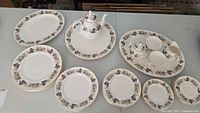 Tea and dinnerware set arranged on table showing teapot, plates, cups, serving plate, and platters with the grape and fruit motif.