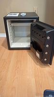 Black SentrySafe safe with electronic keypad front door, door opened showing interior shelving and lining.