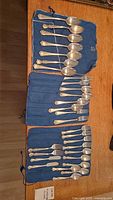 Full view of the flatware set laid out on blue cloth bags showing all forks and spoons in the set.
