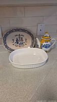 Three-piece kitchen set displayed on countertop including Johnson Bros ironstone platter with Hearts & Flowers pattern, white CorningWare oval baking dish, and blue/yellow ceramic teapot.