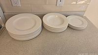 Set of 18 white ceramic dishes: stacked plates and bowls on a light kitchen counter.