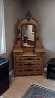 Front view of the antique dresser with mirror in a corner against walls with hardwood floor. Shows full dresser and mirror with drawers and wood finish.