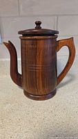 Front side view of wooden coffee pot showing spout, handle and lid with knob.