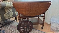 Tea cart angled view showing drop leaf side, turned legs, and lower shelf with decorative wheels