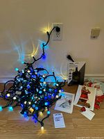Photo showing tangled strings of blue and white Christmas lights plugged in and lit, with holiday cards and timer visible on the floor nearby.
