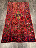Full view of rectangular Persian rug showing overall geometric pattern and colorful border on wood floor.