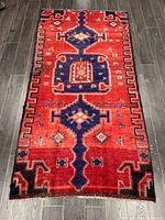 Full view of red Persian rug with dark blue and cream multi medallion geometric design laid on dark floor.