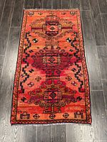 Full view of the rug laid flat on dark wooden floor showing the overall multi medallion geometric design in warm orange and red tones.