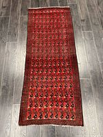 Full length view of the handmade Turkmen rug on a grey wood floor, showing the red and black all-over design.