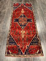 Full view of the rectangular Persian rug with medallion design on a wood floor showing overall condition and size.