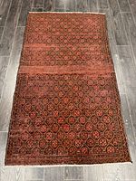 Full view of the Baluch handmade rug laid flat on wood flooring showing the entire geometric pattern and fringe edges.