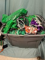 Large plastic bin filled with various Xbox 360 power supplies, cables, and controllers wrapped in protective green packing material.