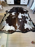 Overall view of a dark brown and beige cowhide rug laid flat on a wood floor, showing its size and pattern.