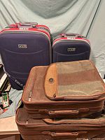 Four pieces of luggage including two navy Polo suitcases stacked behind two brown fabric suitcases.