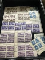 Photo of a box containing multiple blocks and strips of unused Canadian stamps with maritime scenes and portraits