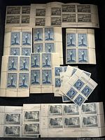 Photo showing multiple blocks and sheets of unused Canadian stamps featuring torch design and industrial scene.