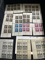 Photo of multiple sheets of unused Canadian stamps in brown, blue, and magenta featuring portraits.