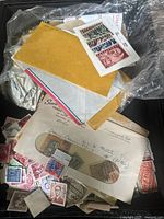 Photo showing a pile of envelopes, loose stamps, and a plastic sleeve containing a sheet of stamps with various colors and denominations.