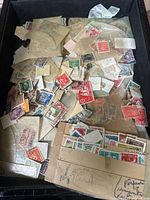 Used postage stamps in a black container with various stamps loose and on paper pieces.