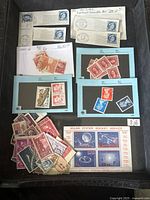 Photo of used and unused stamps in envelopes, blue stock cards with sets of stamps, and mixed pile of loose stamps including a Solar System Rocket Service sheet