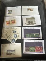Overhead photo showing multiple stamps mounted on cards with handwritten catalog numbers and notes, including used and unused examples.