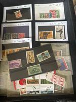 Overview showing various used and unused stamps on black pages and loose in plastic sleeves with catalog prices and selling prices visible.