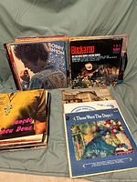 Photo showing a stack of vinyl records with visible titles including Bobby Vinton's Melodies of Love, Buckaroo album and others, placed on a fabric background.