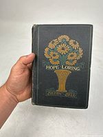 Front cover of the 1902 book 'Hope Loring' showing floral decoration and title with author name Lillian Bell.