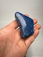 Polished lapis lazuli specimen held in hand showing deep blue color with natural white and lighter blue vein patterns, irregular shape with smooth finish.