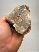 Hand holding an irregularly shaped chunk of agate showing natural banding and a small cavity with crystal formations.