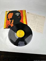 Photo showing album cover featuring Andy Warhol style pop art of silhouette in black and orange, vinyl record, and album insert with text.