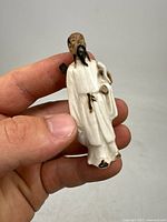 Photo showing the front view of a small hand-held antique Chinese Mudman figurine depicting a sword warrior dressed in white robes, holding a sword.