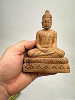 Front view of the hand showing the wooden Buddha statue seated on a lotus base, detailing the facial features and robe folds