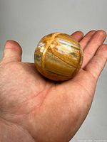Hand holding a polished orange and white banded onyx sphere showing natural patterns and glossy finish.