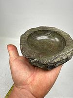 Carved stone dish held in hand showing top view, polished concave interior, and rough textured edges.