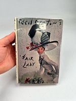 Front cover of Cecil Beaton's Fair Lady book showing illustrated woman with detailed hat and title text.