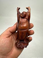 Front view of the carved Hotei Buddha statue held in hand, showing the detailed carving and wood grain.