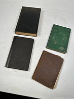 Four antique hardcover school books from the late 1800s to early 1900s, arranged on a white surface showing general wear and use.
