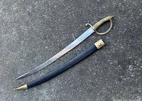 French Briquet saber sword with brass handle and black leather scabbard laid out on concrete surface.