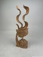 Full view of the wooden statue with twisted, flowing abstract shapes rising from a sculpted base with carved face details.