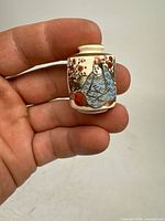 Mini Japanese Satsuma-style vase held between fingers showing front detailed hand-painted figure and decoration