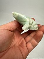 Front view of the carved stone frog showing green and white banding with clear detail of the eye and smooth contours.