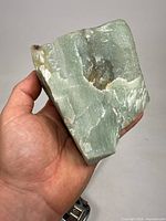 Photo showing the front view of the large chunk of natural jade, highlighting the rough texture, green color with white streaks, and natural inclusions.