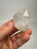 Clear rock crystal quartz point held between thumb and fingers; shows natural crystal shape and termination facets.
