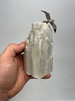 Front view of the large selenite crystal resembling a cliff with a bird sculpture on top held in hand for scale.