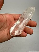 Photo of clear polished quartz crystal specimen held in hand showing size and details