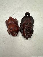 Two fruitwood carved masks depicting a man and a woman, photographed on a white surface.