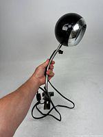 Black Mid-Century Modern orb lamp with clamp base, flexible neck, and chrome trim, shown held in hand to indicate size