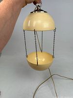 Full view of hanging orb lamp showing the two cream-colored hemispherical metal shades connected by black chains with electrical cord attached.