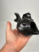 Black clay pottery fish shown in hand at side angle to display detail and size